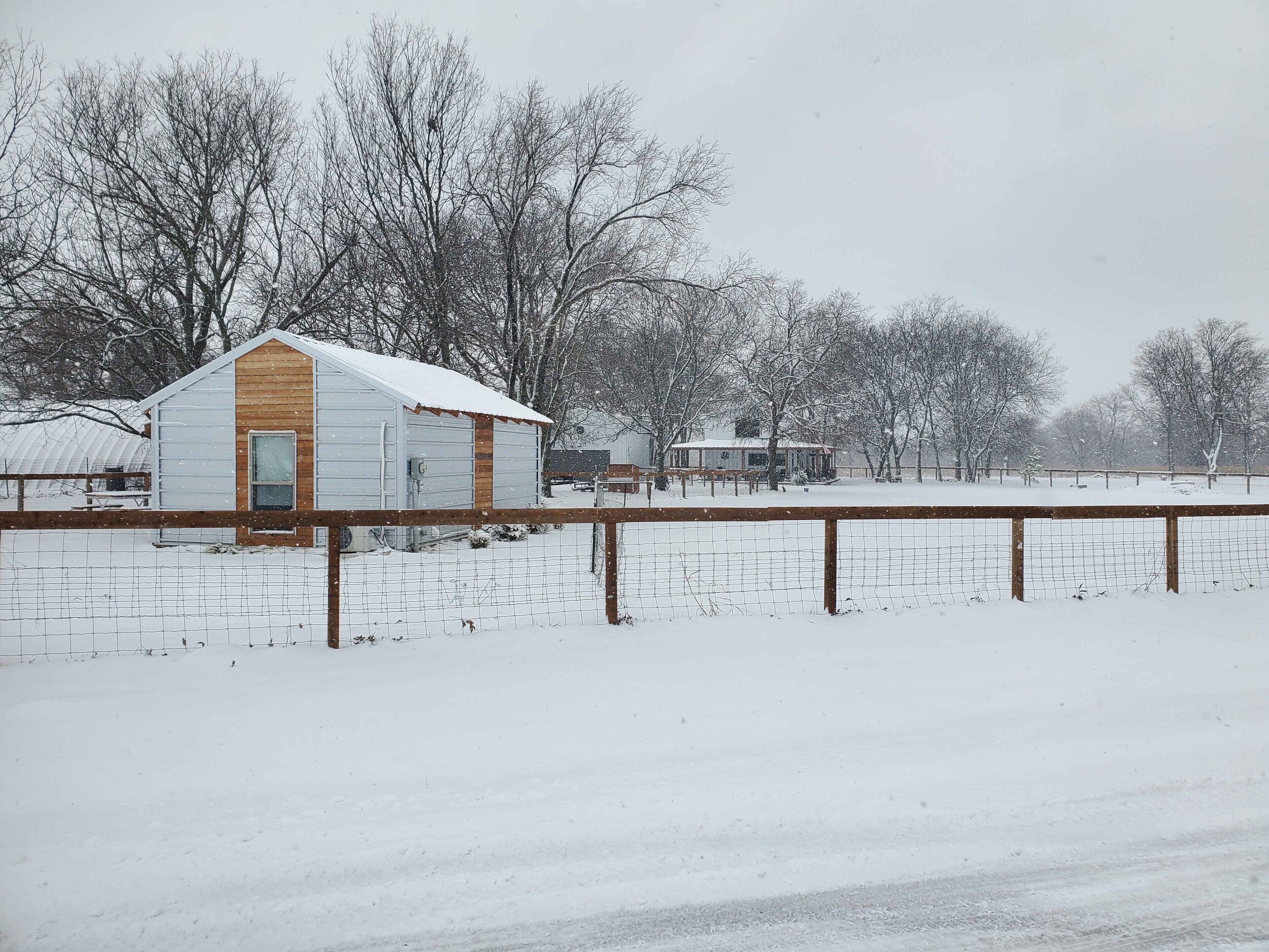 A snow-covered rural landscape with a small wooden barn and a metal shed.