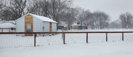 A snow-covered rural landscape with a small wooden barn and a metal shed.