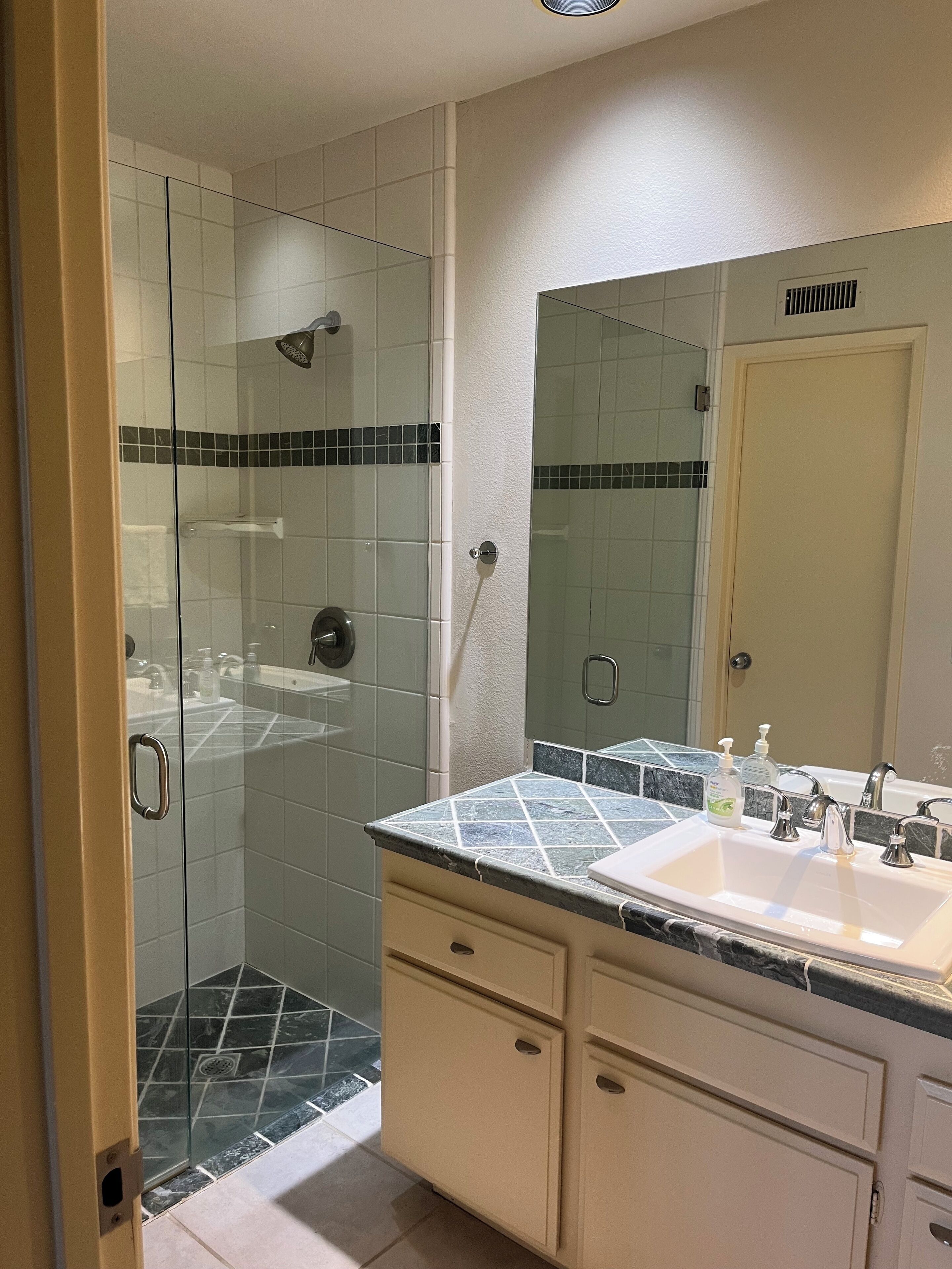 A bathroom with a glass-enclosed shower, a sink with a marble countertop, and a mirror above the sink.