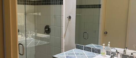 A bathroom with a glass-enclosed shower, a sink with a marble countertop, and a mirror above the sink.