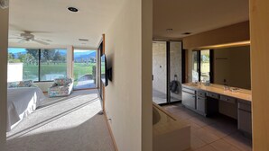 Ein Schlafzimmer mit großem Fenster, Deckenventilator und Blick auf eine grüne Landschaft.