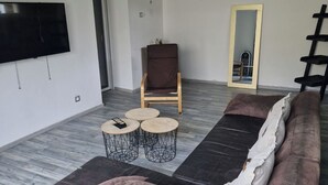 Una sala moderna con un televisor de pantalla plana grande, un sillón marrón, un sofá con un cojín rasgado y un espejo en la pared.