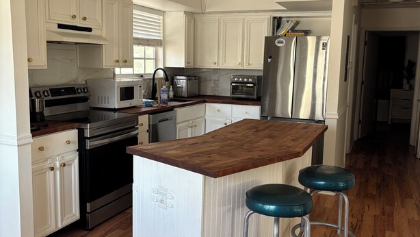 A modern kitchen with white cabinets, stainless steel appliances, a wooden island with bar stools, and a ceiling fan. - 5 Minute Walk to Beach, Restaurants, Shops,Playground. Quaint and Quiet in IRB ! (Indian Rocks Beach)
