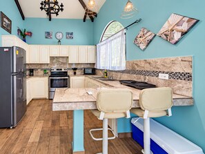 A modern kitchen with white cabinets, a marble countertop, and a dining area with two chairs.