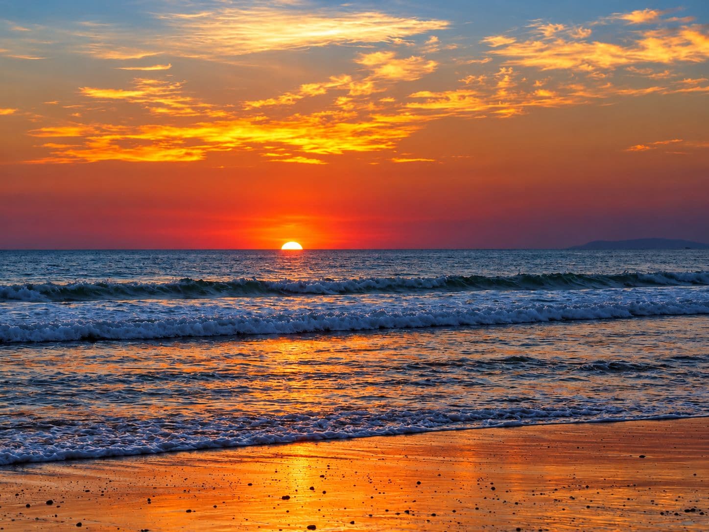 Ein Sonnenuntergang über dem Meer, wobei Wellen auf das Ufer zurollen.