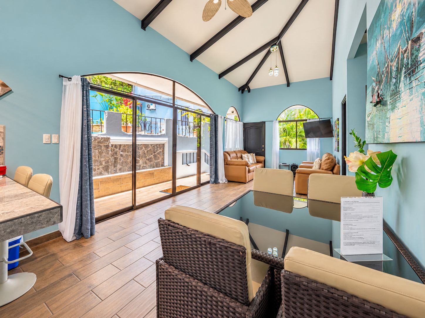 Uma sala de estar moderna com divisória de vidro, sofás de couro, uma mesa de jantar e uma janela grande com vista para o verde.