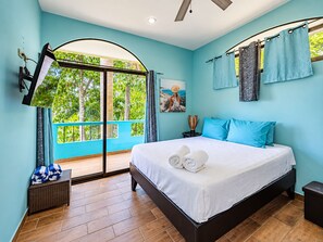 A bedroom with a bed, a window with curtains, a ceiling fan, and a view of greenery outside.