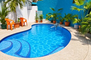 A swimming pool with a blue tiled edge, surrounded by potted plants and orange chairs. - 7BR · 2 Homes · Sleeps 16 · Pool ·  Walk to Jacó Beach (Jaco)