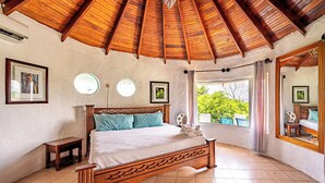 Une chambre à coucher avec un lit en bois, une petite table de chevet et une grande fenêtre avec des rideaux.