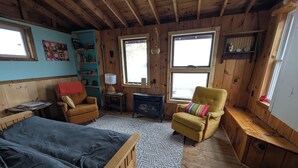 Ein gemütliches Cabin-Zimmer mit einem Bett, einem gelben Sessel, einem kleinen Tisch und einem Bücherregal.