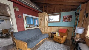 Ein gemütliches Blockhaus-Interieur mit einer Holzbank, einem gemusterten Teppich, einem kleinen Sessel, einem Tisch mit Lampe und einem Kamin.