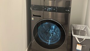 A stacked washer and dryer unit with a control panel and a small trash bin beside it. - New, spacious and lovely two-bedroom basement suite in a peaceful neighbourhood  (Calgary)