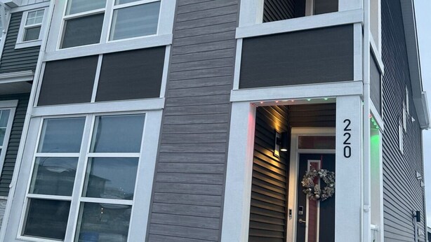 A two-story building with a dark gray and white exterior, a visible number '220' on the front, and a small porch area. - New, spacious and lovely two-bedroom basement suite in a peaceful neighbourhood  (Calgary)