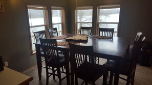 A dining room with a rectangular table surrounded by six chairs. The room has large windows with blinds partially drawn, allowing natural light to enter. - 5-bedroom house in Edwards with AC, WiFi,lakefront, beautiful view, private dock (Edwards)