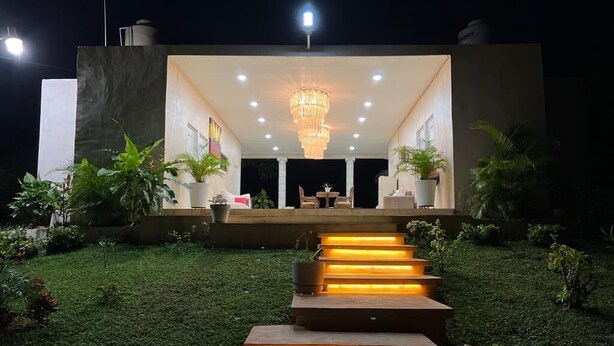 A modern outdoor seating area with a chandelier, steps leading up to it, and potted plants. - Quinta Yaaxbe (Homún)