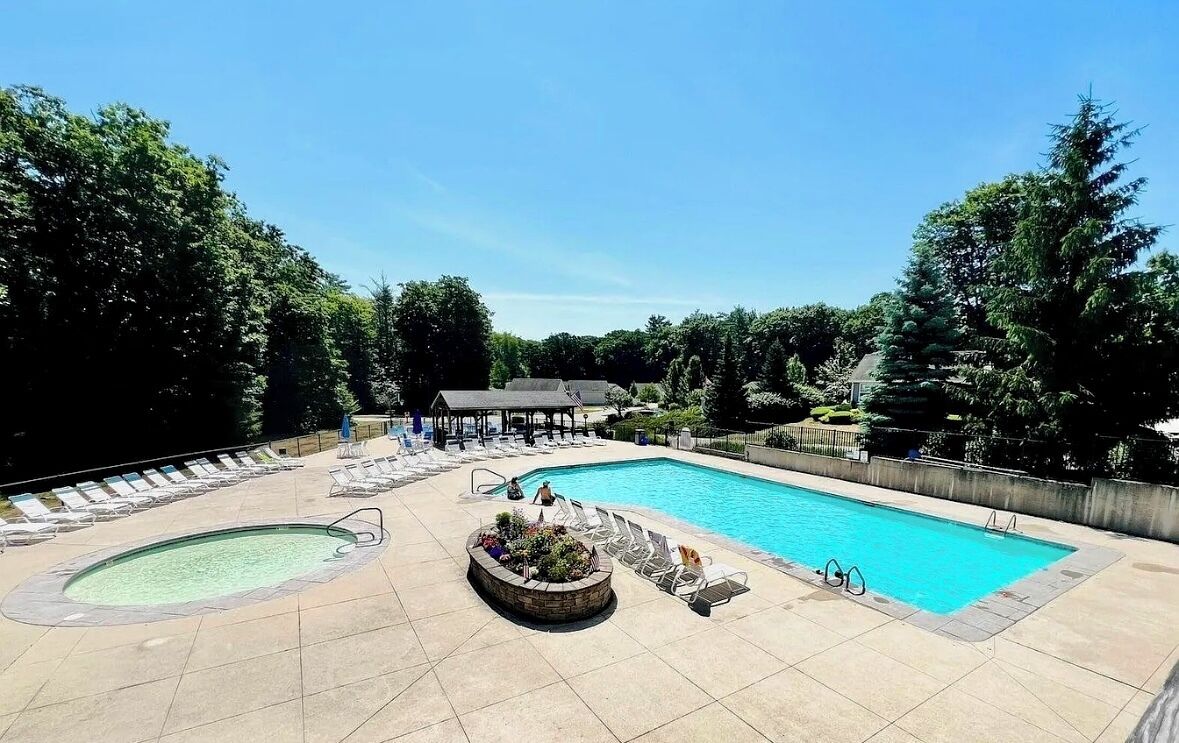 A swimming pool with lounge chairs and a covered area, surrounded by trees.