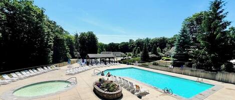 A swimming pool with lounge chairs and a covered area, surrounded by trees.
