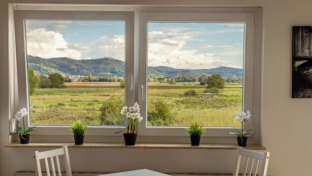 A room with a large window overlooking a rural landscape, a table, and two chairs.