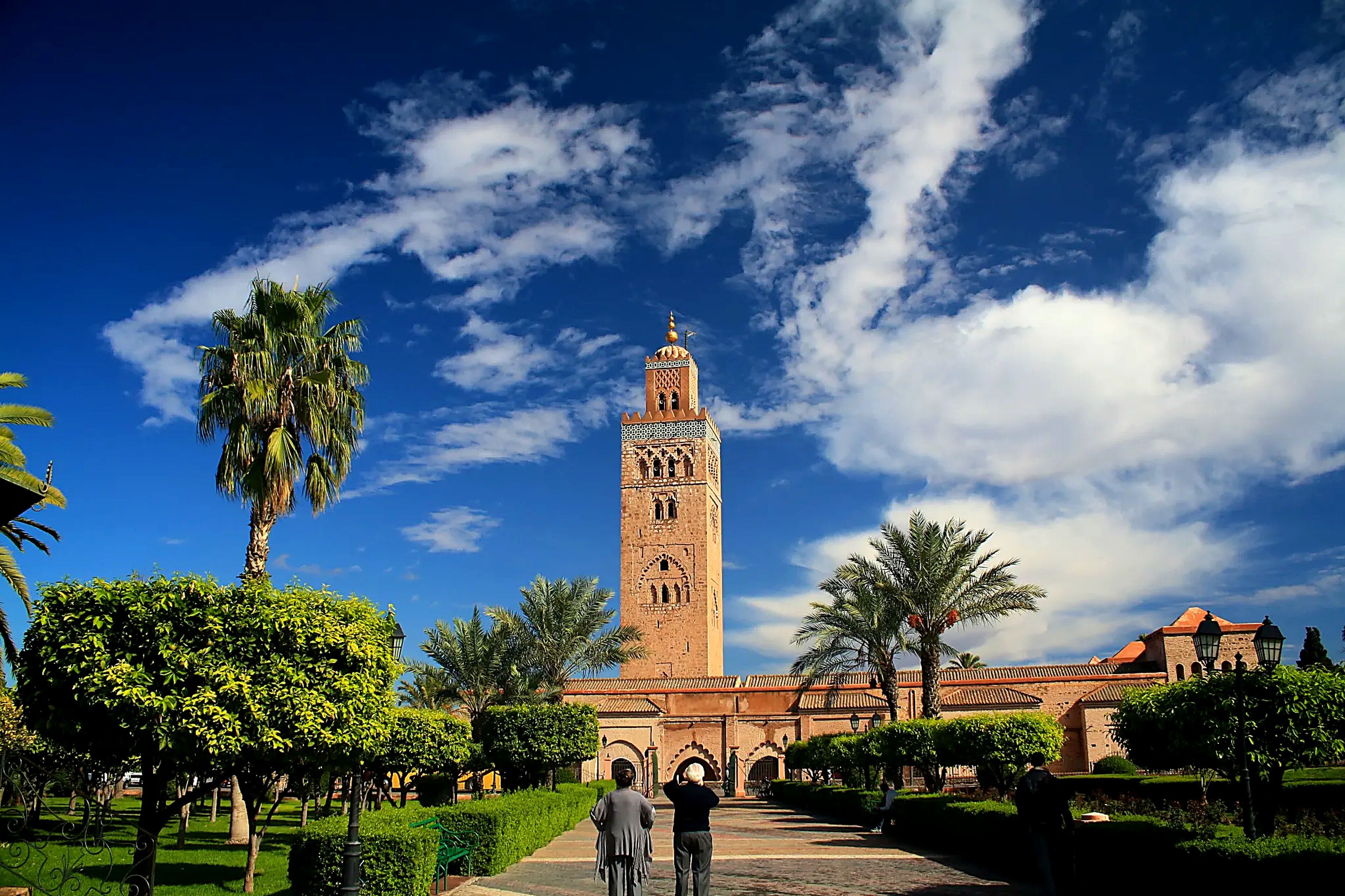 A historic building with a prominent tower, surrounded by well-maintained greenery and a clear blue sky.