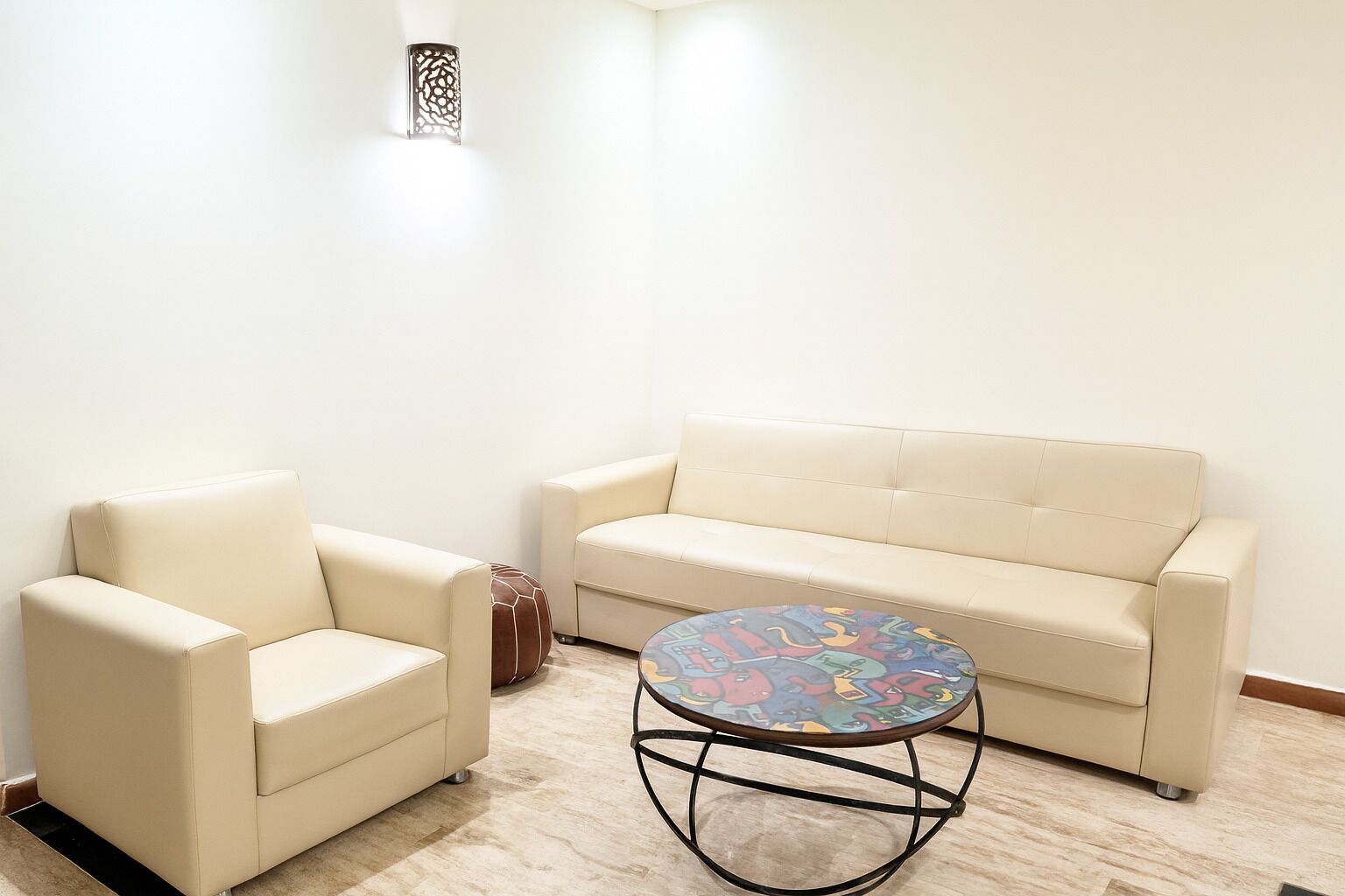 A room with a beige sofa, a matching armchair, and a small round table with a colorful pattern.