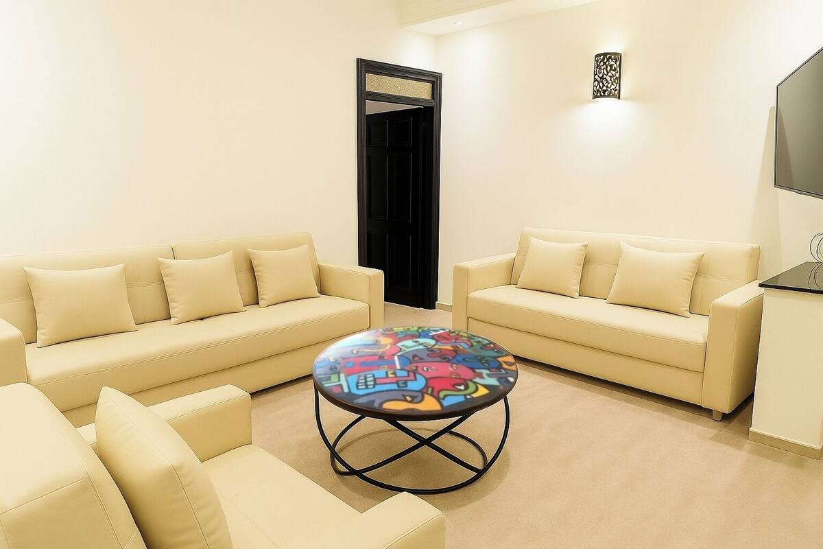 A modern living room with two beige sofas, a round coffee table with colorful patterns, and a black-framed door.