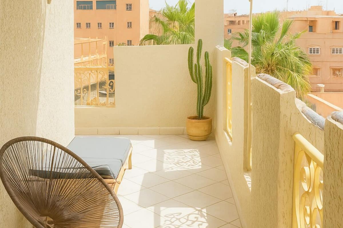 A balcony with a wrought iron railing, a cactus plant, a wicker chair, and a small table.