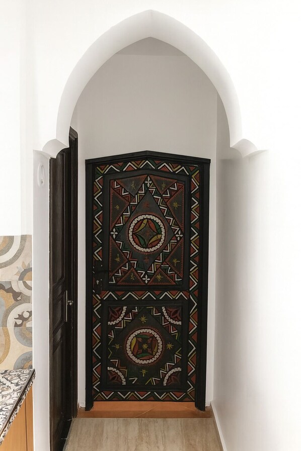 Una puerta con intrincados diseños geométricos y un motivo circular central, ubicada en un pasillo con un arco blanco y suelo de baldosas.