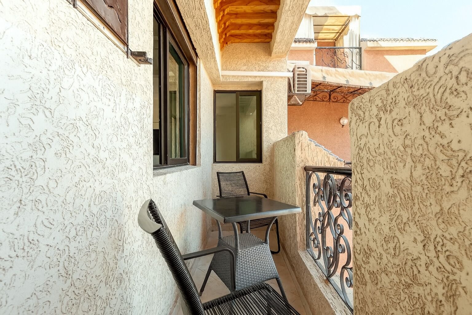Un balcón con una mesa, dos sillas, un ventanal y una baranda decorativa.