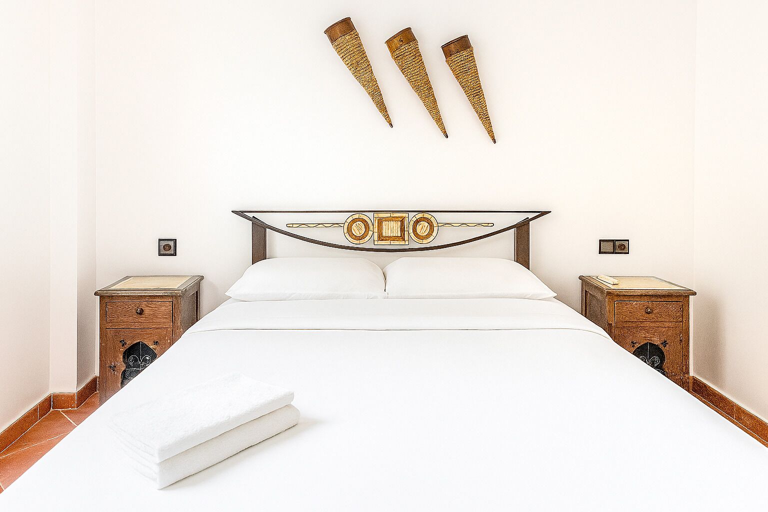 A neatly made bed with white linens, two bedside tables with lamps, and a decorative wall piece above the bed.