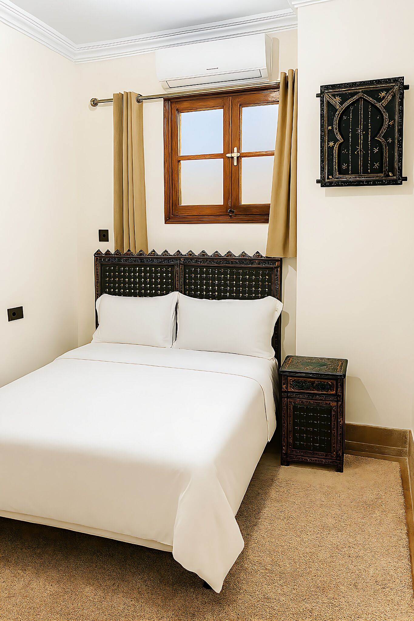 A neatly made bed with a wooden headboard, a small bedside table, and a window with curtains.