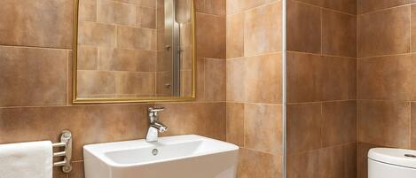 A bathroom with a white sink, a mirror with a gold frame, and brown tiles.