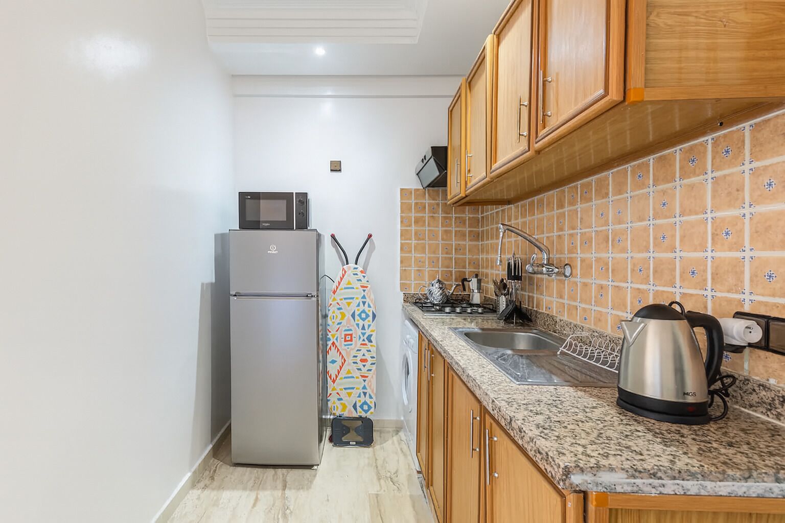 Una cocina compacta con refrigerador, microondas, pileta y salpicadero de azulejos.