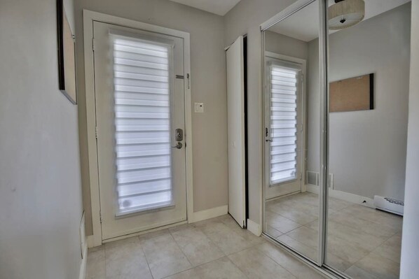 Um corredor com uma porta e uma porta de correr de vidro, ambos com persianas brancas.