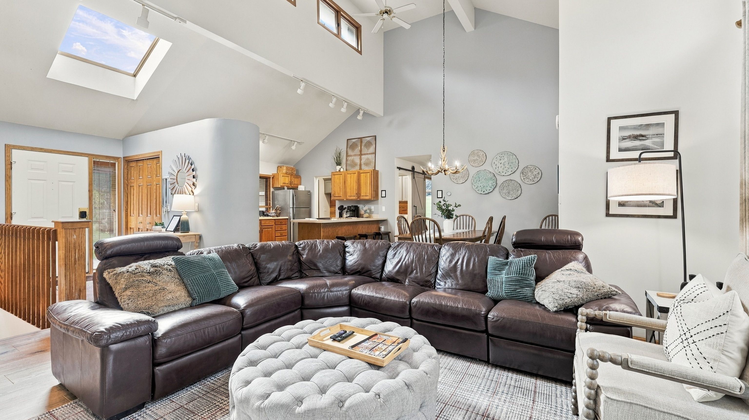 Una sala moderna con un sofá modular, un reposapiés y una zona de comedor con muebles de madera.