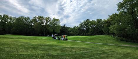 A golf course with a clear sky, lush green grass, and trees in the background.