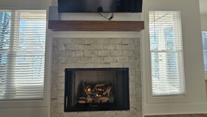 A living room with a fireplace, a flat-screen TV mounted above it, and two windows with blinds. - New lakefront 3 bedroom, 2 story house in lovely Georgetown with private dock (Georgetown)
