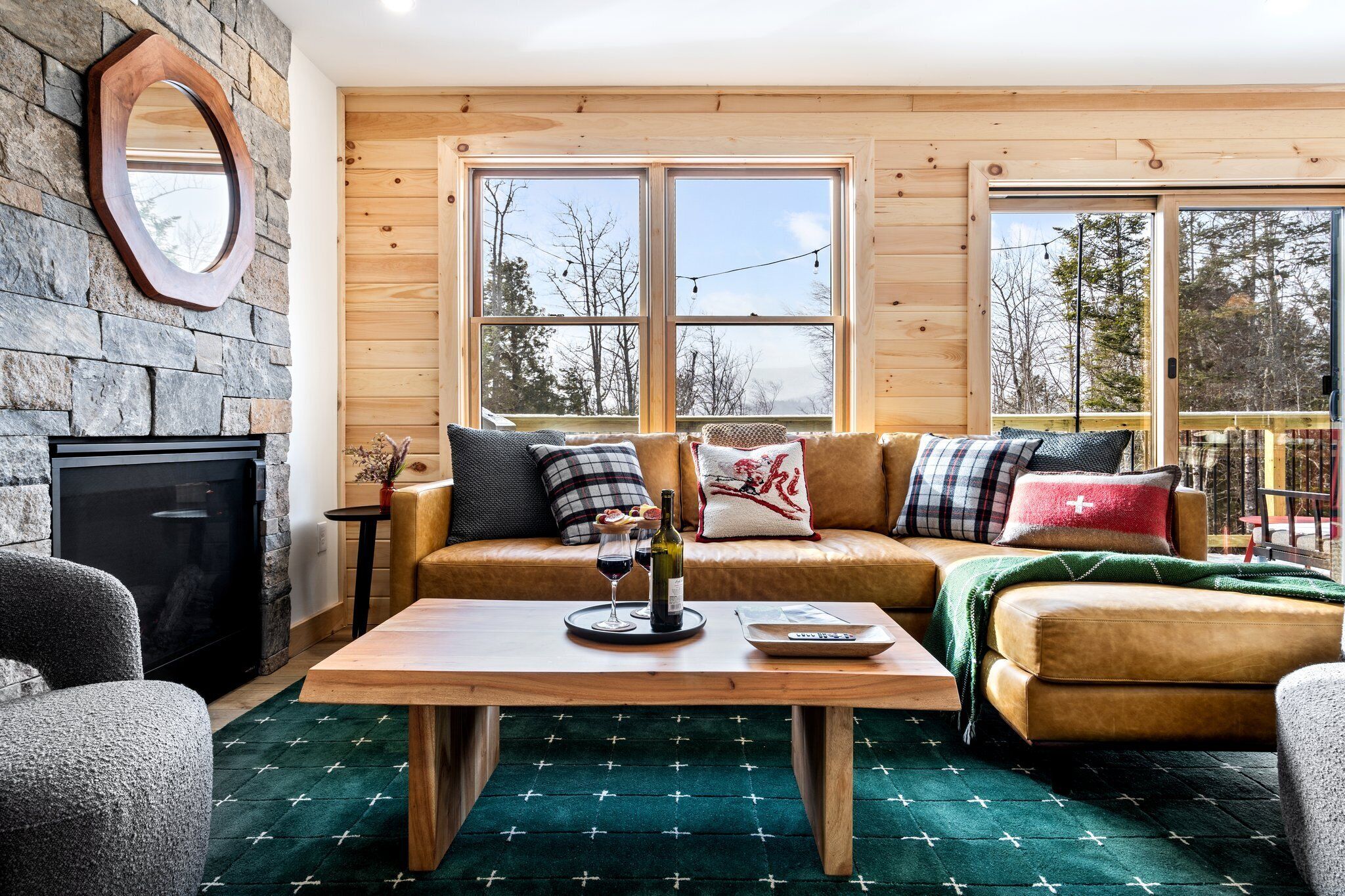 A cozy living room with a stone wall, wooden ceiling, and large windows.