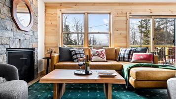 A cozy living room with a stone wall, wooden ceiling, and large windows.