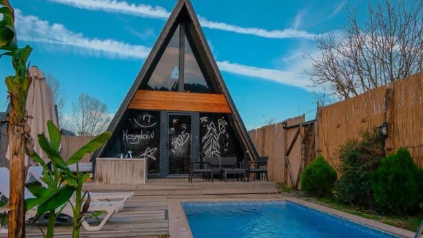 Une maison moderne avec un toit triangulaire, une piscine et une terrasse en bois.