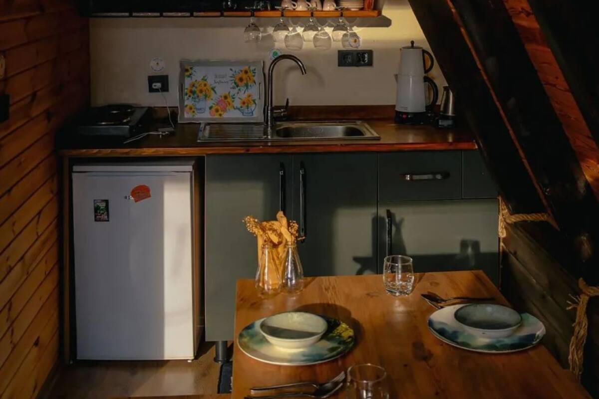 A compact kitchen with wooden walls, a small refrigerator, and a dining table set for two.