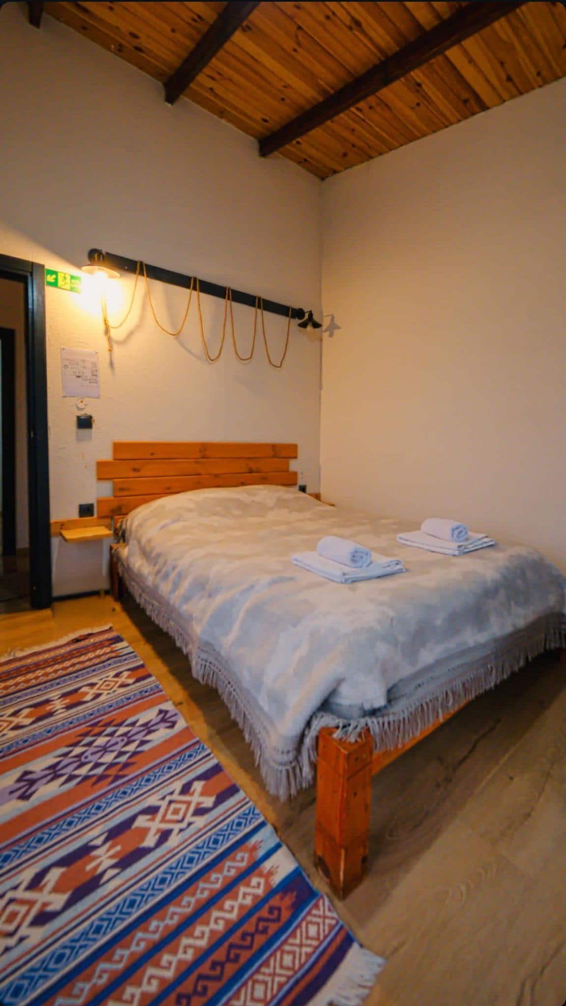 Une chambre avec un lit en bois, un tapis à motifs et un plafond en bois.