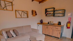 Un salon chaleureux avec un plafond en bois, un canapé, une table basse et un coin cuisine équipé de placards et d’un extincteur.