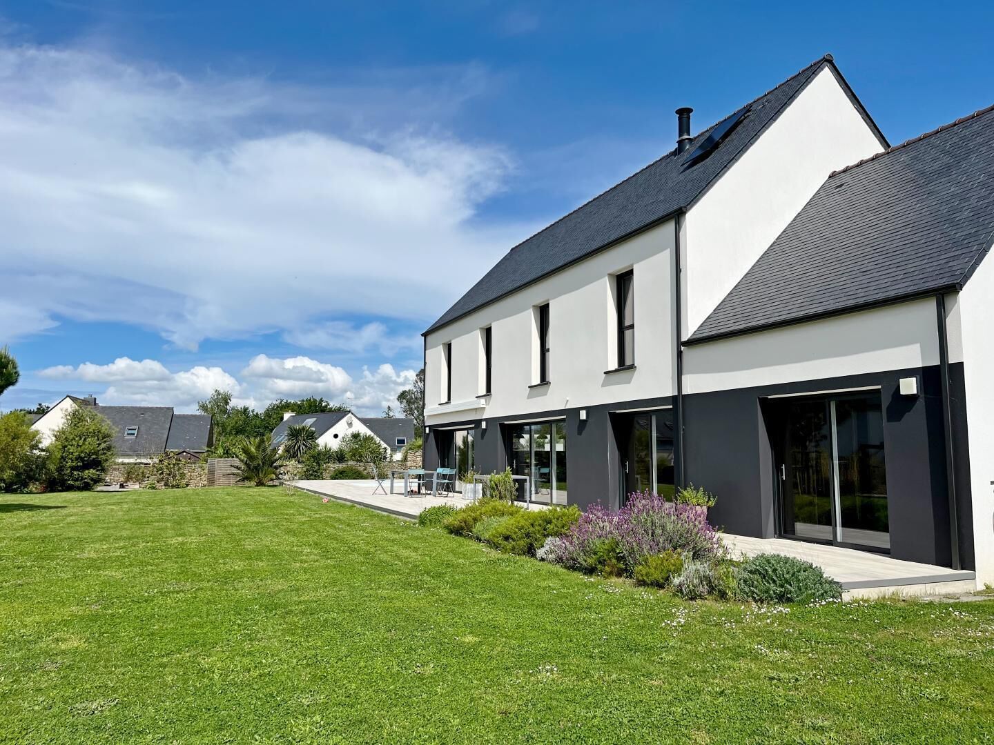 A modern two-story house with a large lawn and a patio area.