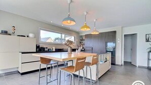 Una cocina moderna con una isla central, taburetes de bar, iluminación colgante y vistas al exterior.
