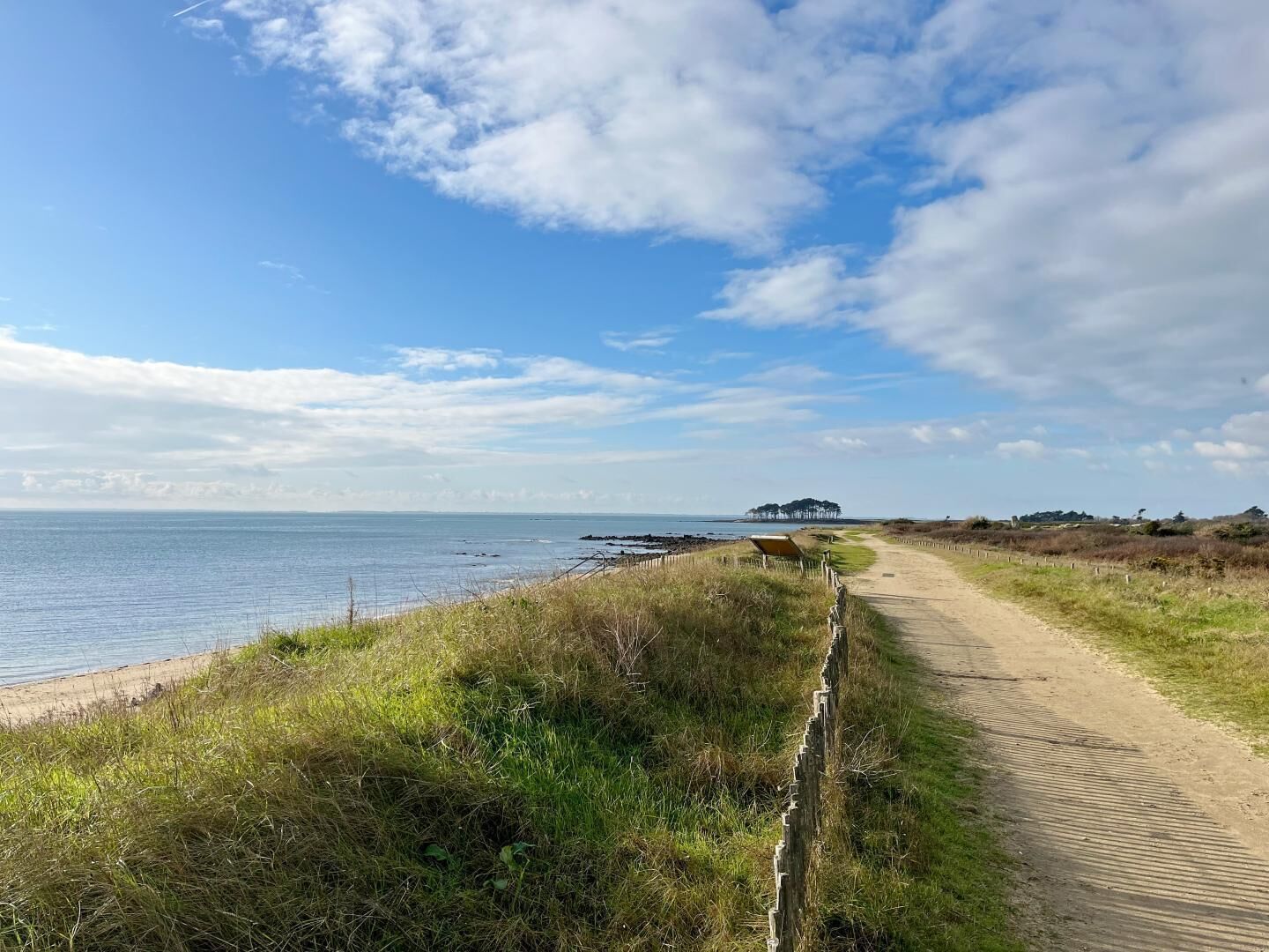 A coastal path leading to a beach with a wooden fence and a distant structure.