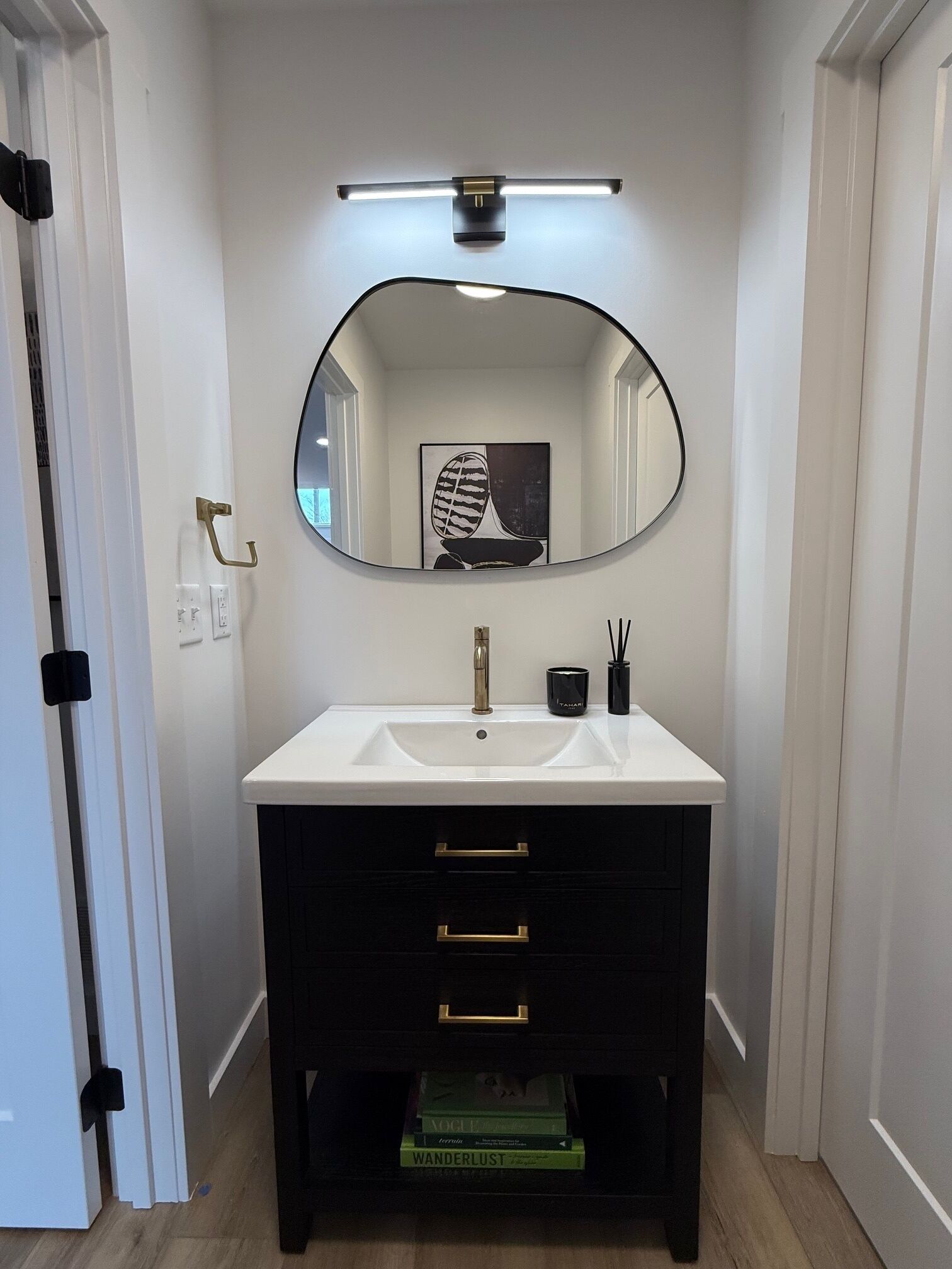 A bathroom with a white sink, a black vanity, a mirror, and a framed artwork above the mirror.