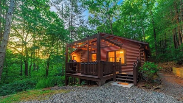 A log cabin with a porch, surrounded by dense forest. - Romantic Cabin + Hot Tub + Firepit (Ellijay)