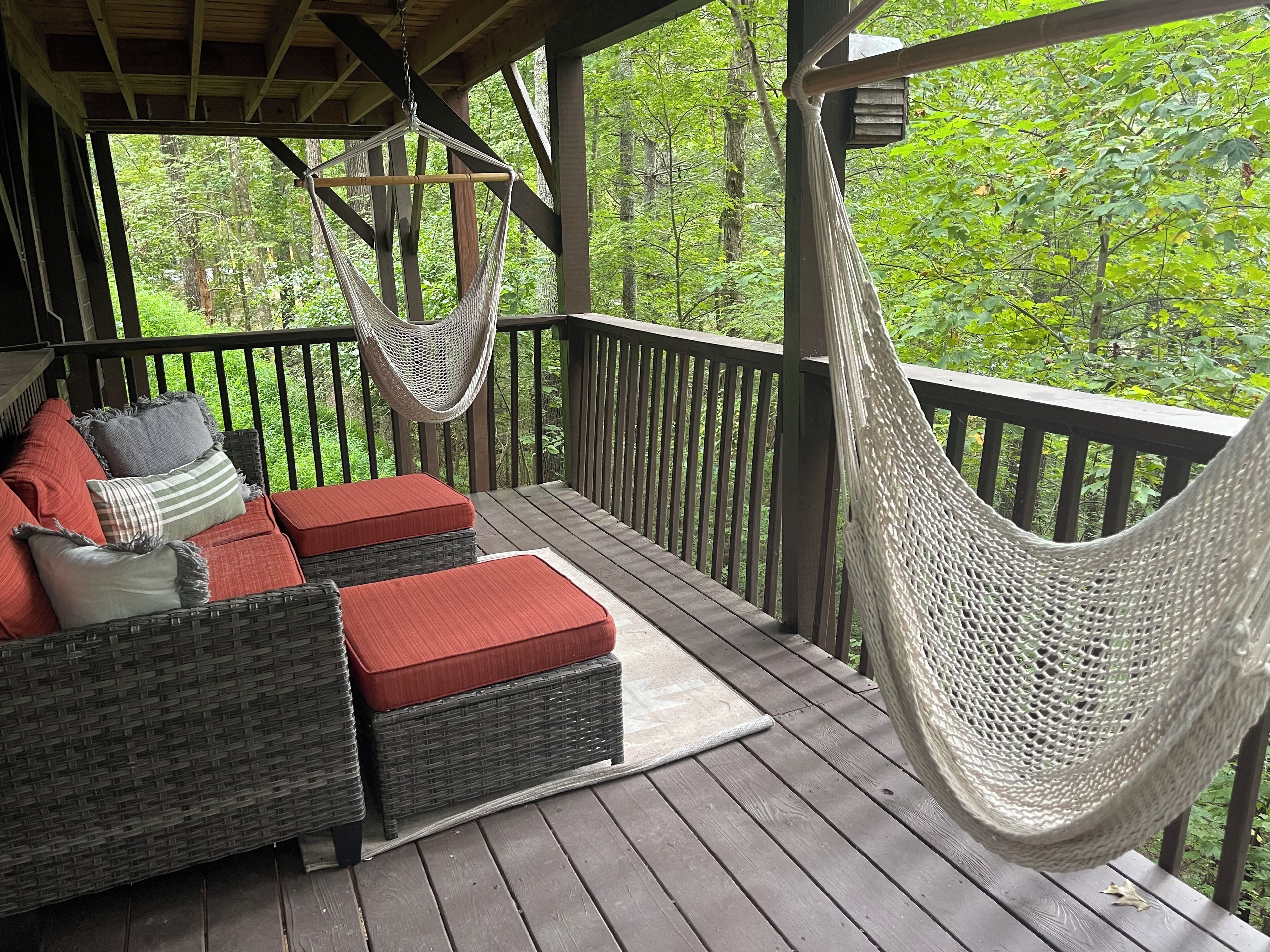 A covered porch with wicker furniture, a hammock, and a view of a forest.