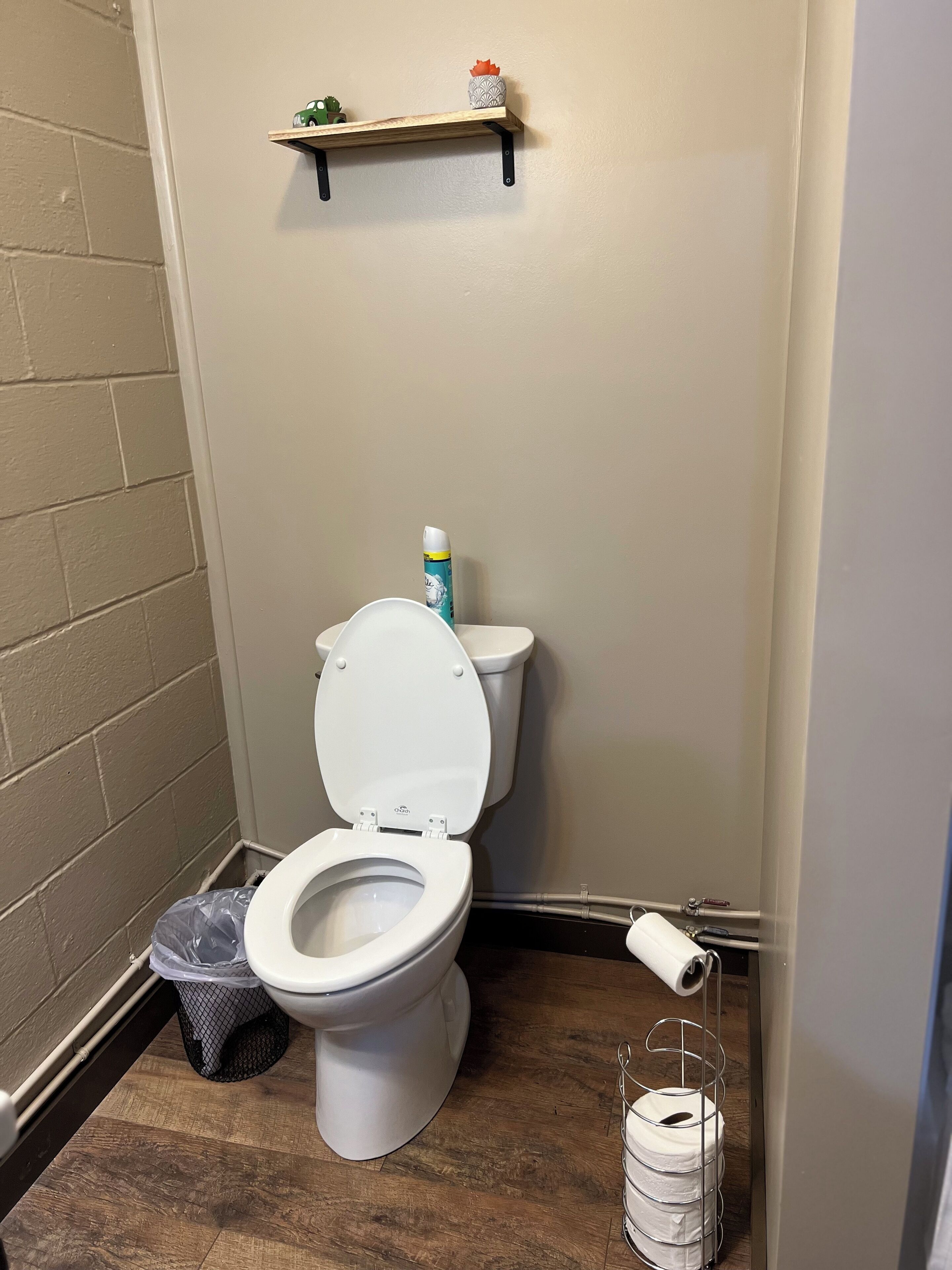 Pieni kylpyhuone, jossa on wc-istuin, wc-istuimen yläpuolella oleva hylly, roskakori ja wc-paperiteline.