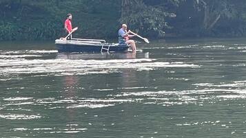 Una barca con dos personas remando en un río tranquilo rodeado de abundante vegetación.